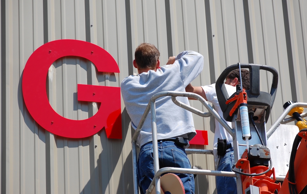 A sign installation crew is installing a sign at a warehouse.